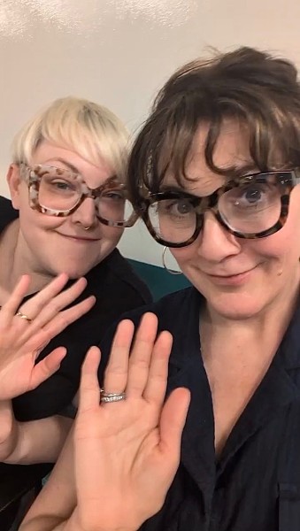 Two women laughing at a women-in-AI meetup, hands raised, captured in a selfie